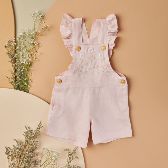 Niño sonriente vistiendo overoles cortos rosados y camiseta blanca con estampado gráfico