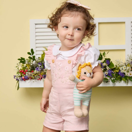 Niño sonriente vistiendo overoles cortos rosados y camiseta blanca con estampado gráfico