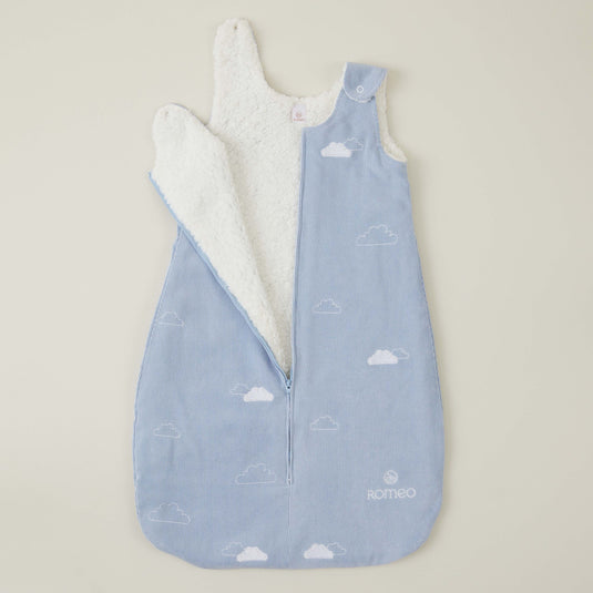Bebé acostado dentro del saco de dormir con estampado de nubes y cielo.